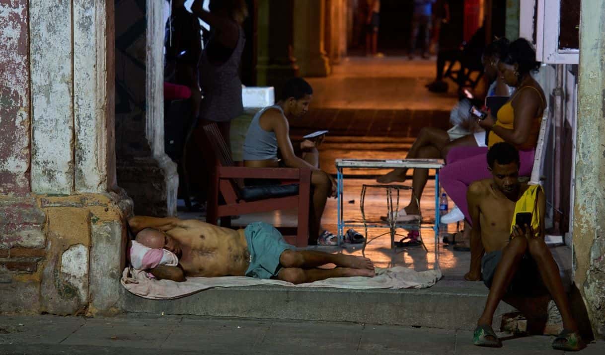Un hombre duerme en la puerta de su casa mientras otros pasan el tiempo tratando de refrescarse en la calle en La Habana, Cuba, el martes 4 de agosto de 2026. (AP Foto/Ramón Espinosa)